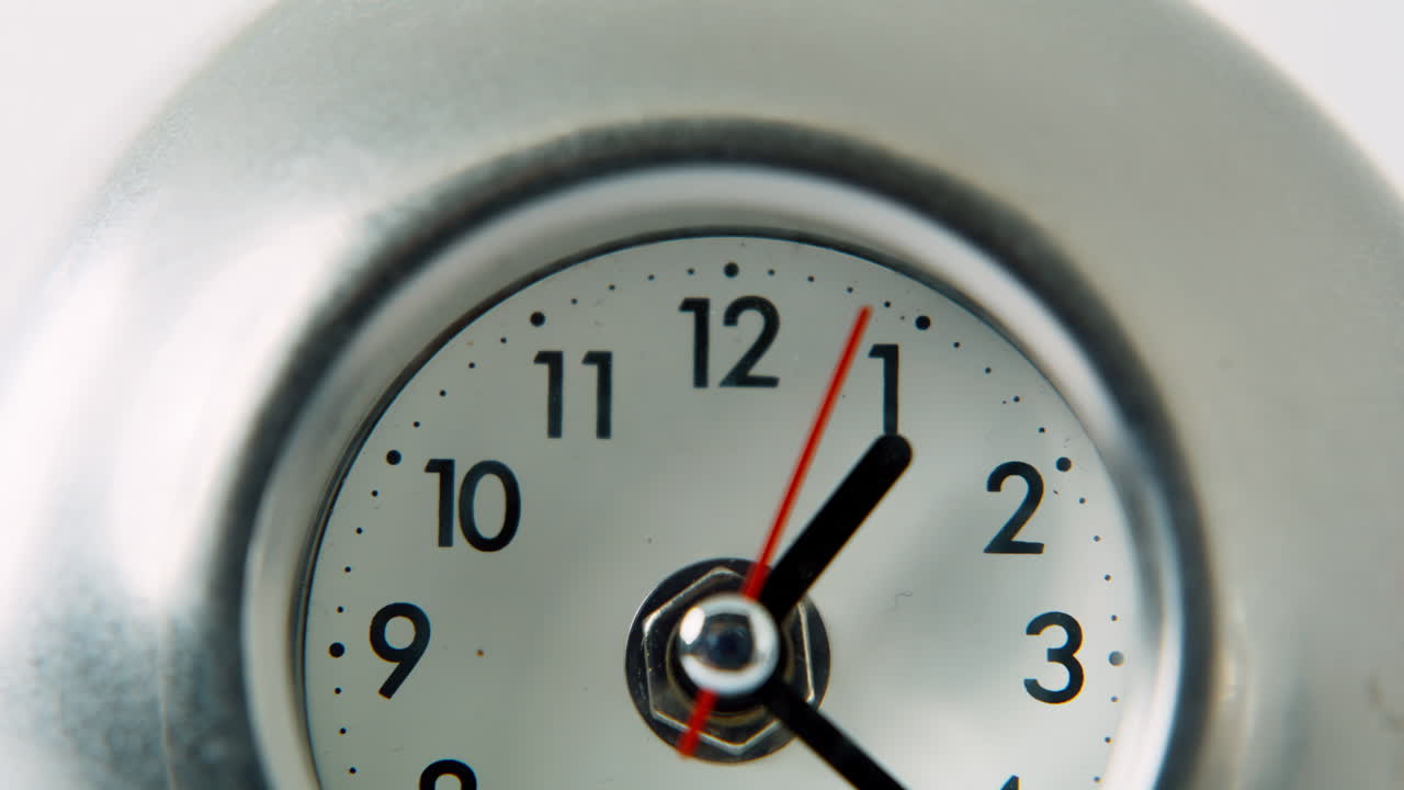 Macro mechanical clock moving hands on silver surface in room. Circular object