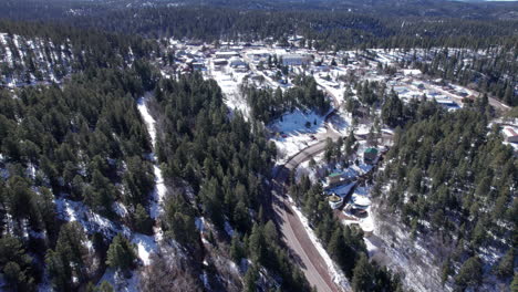 drone aerial of a snowy mountain highway, cars drive along a coniferous forest