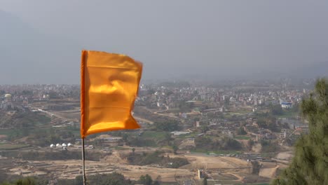 an orange hindu flag flapping in the wind at a temple overlooking the city of kathmandu, nepal