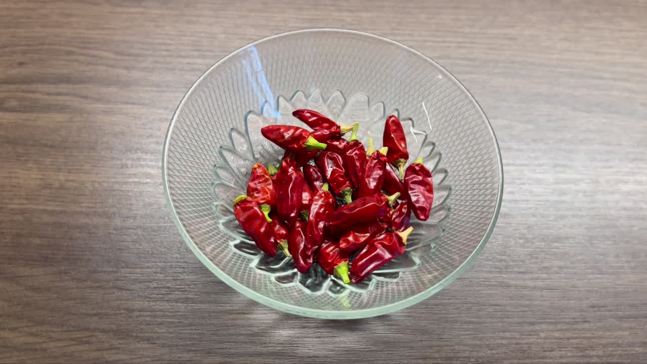 Red hot chili peppers in glass bowl, rotation on wooden desk
