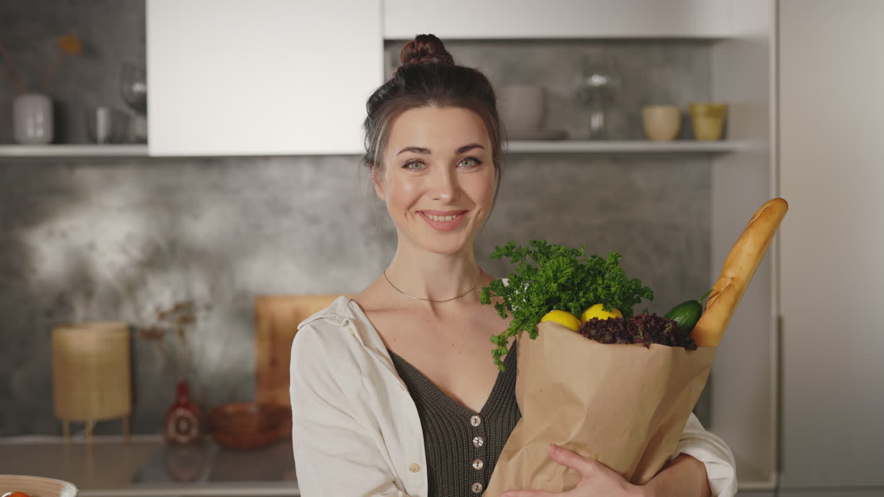 Mujer sonriente sosteniendo una bolsa de papel con la compra en una cocina moderna