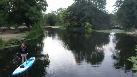 Paddle-boarding-at-sunrise-at-Flatford,-Suffolk,-England-along-the-river-stour-by-drone