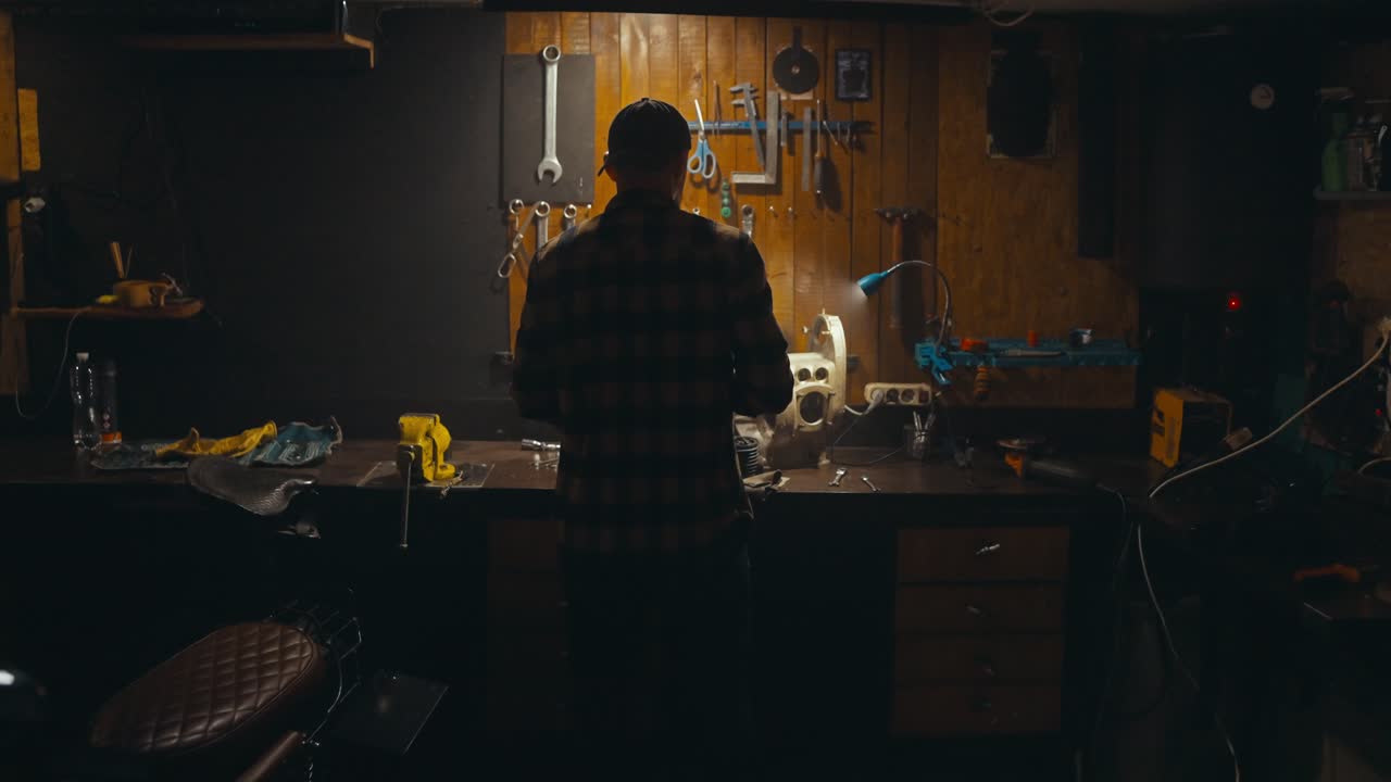 Rear view of a confident guy mechanic working on his workbench and picking up the necessary tools from the rack in his cozy workshop