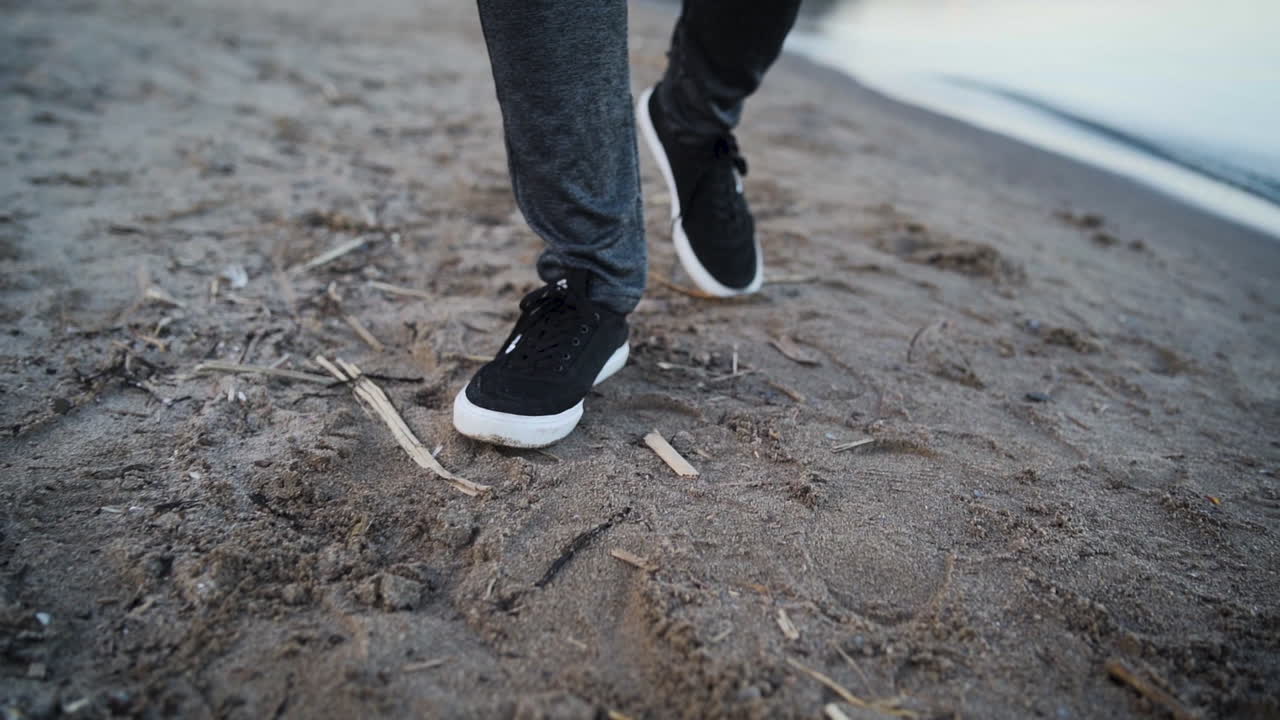 느린 동작으로 해변을 걷고 있는 남자의 발을 클로즈업