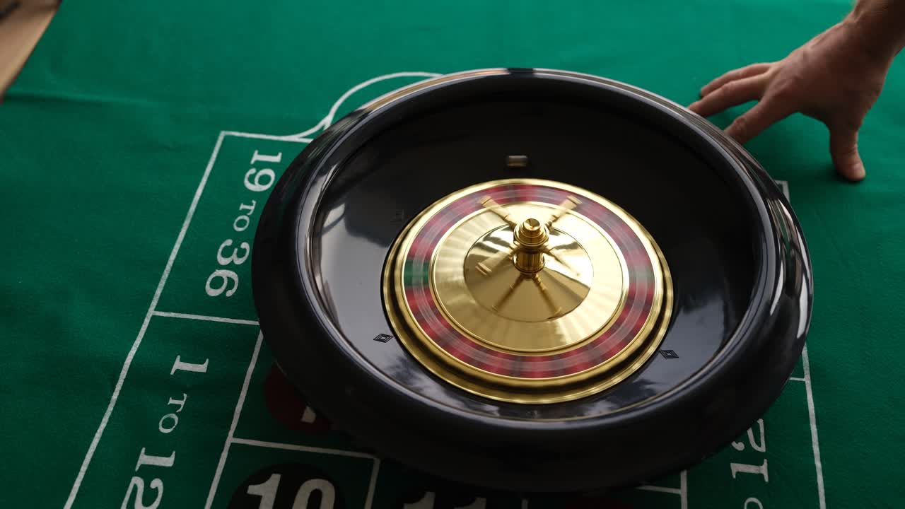 La mano del croupier fa girare la ruota della roulette su un tavolo da casinò verde.