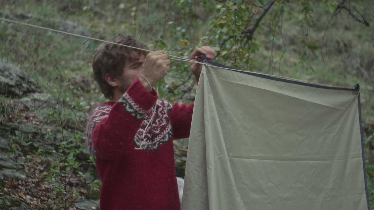 Survivalist Fastening Tent Edge with Rope while Preparing Forest Campsite