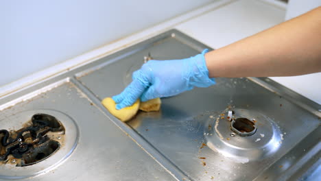 deep clean stove surface. a person wearing blue gloves scrubs a dirty kitchen stove with a sponge, removing grime and residue effectively