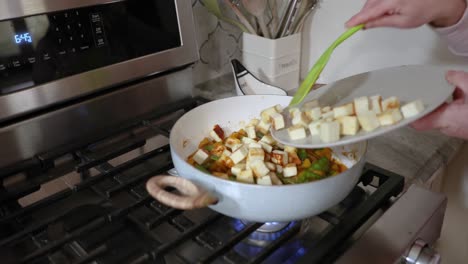 mujer agregando paneer cocido en una sartén de verduras calientes en 4k