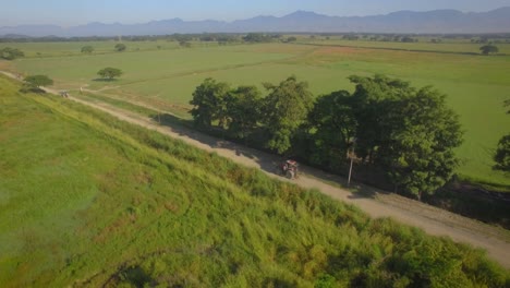 Aerial-video-of-a-tractor-going-on-a-dirt-road-across-the-countryside-field