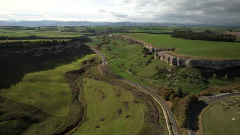 Beautiful-scenic-view-of-road-in-valley-and-limestone-cliff,-farmland,-rural-of-New-Zealand---aerial