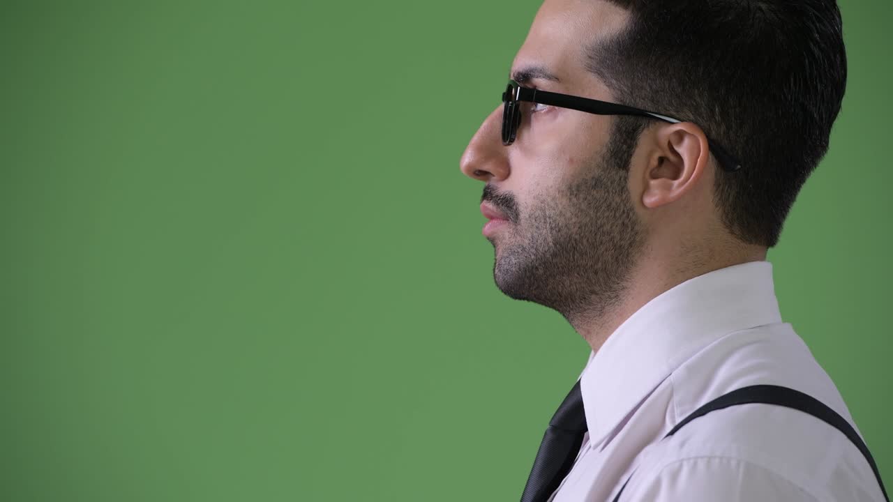 Young handsome bearded Persian businessman against green background