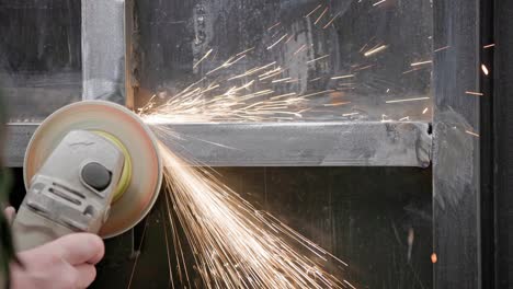 caucasian hand cleaning of welded seams with an angle grinder with a flap disc on welded metal construction close-up with long spark trails, slow motion