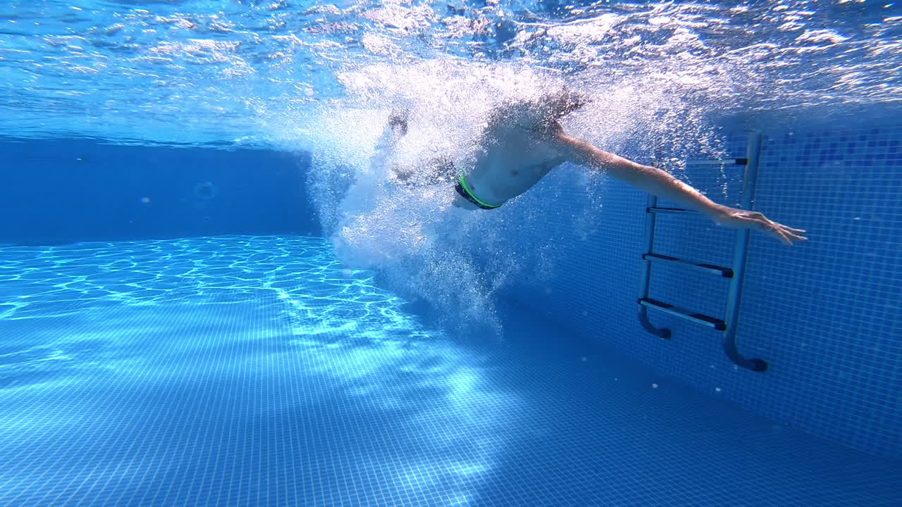 Boy jumping and swimming underwater in the pool. Transparent water background inside the swimming pool and healthy boy swims.
