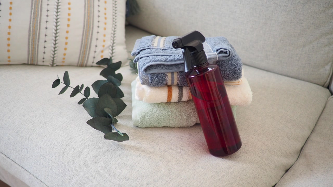 Red Spray Bottle and Stack of Fresh Towels on a Sofa