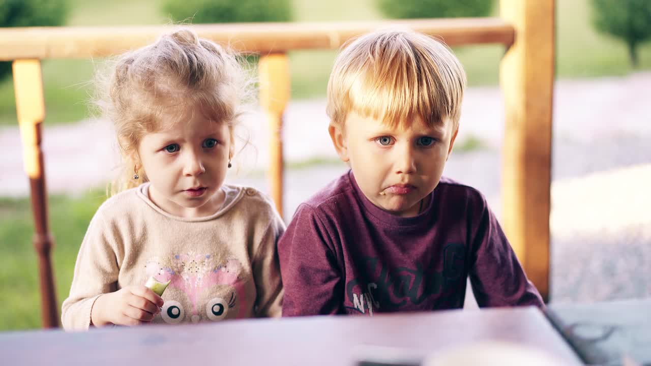 Primo piano: I bambini, seduti nella casetta estiva, mangiano e la mamma li imbocca con le verdure.