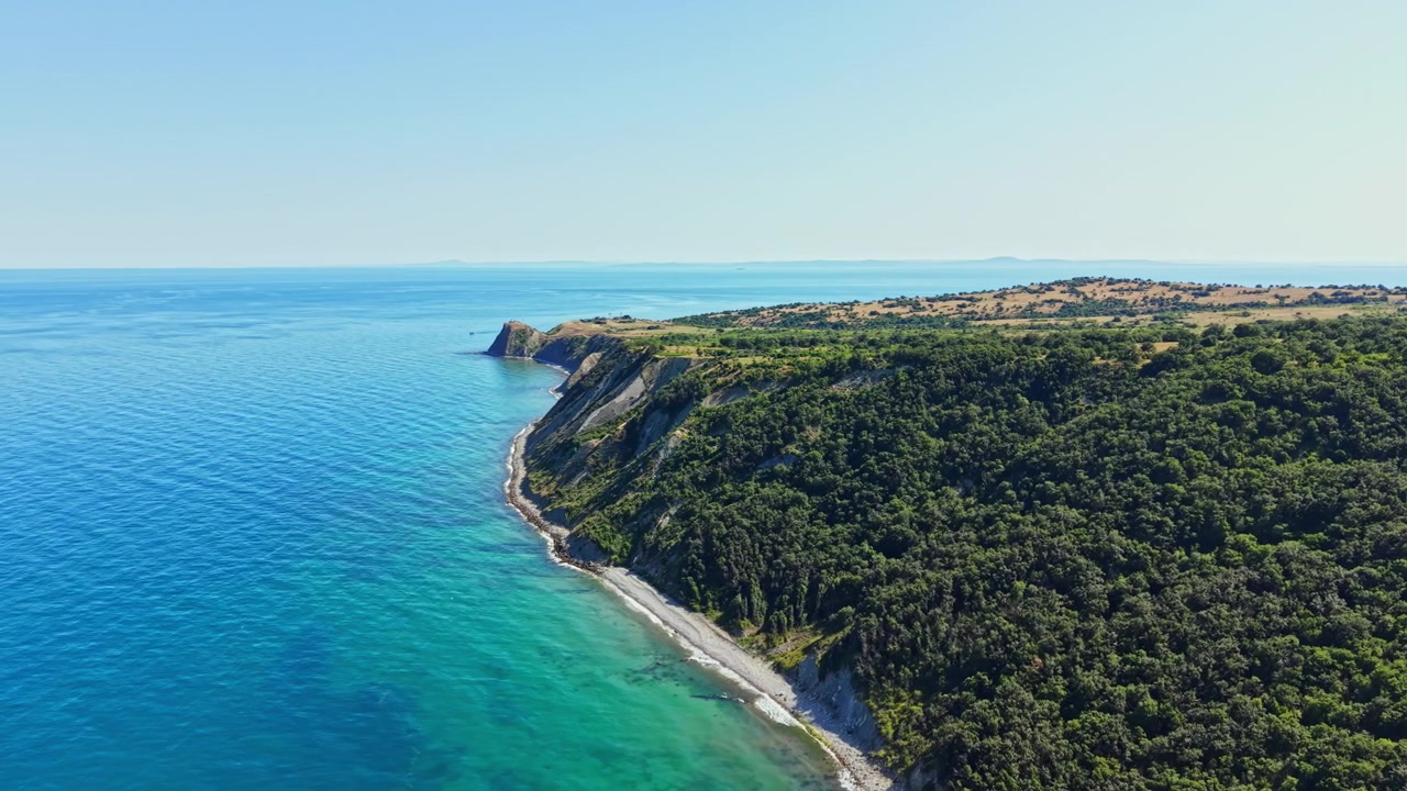Litorale con colline verdi e acqua cristallina che incontra il cielo in una luminosa giornata di sole vicino all'oceano.