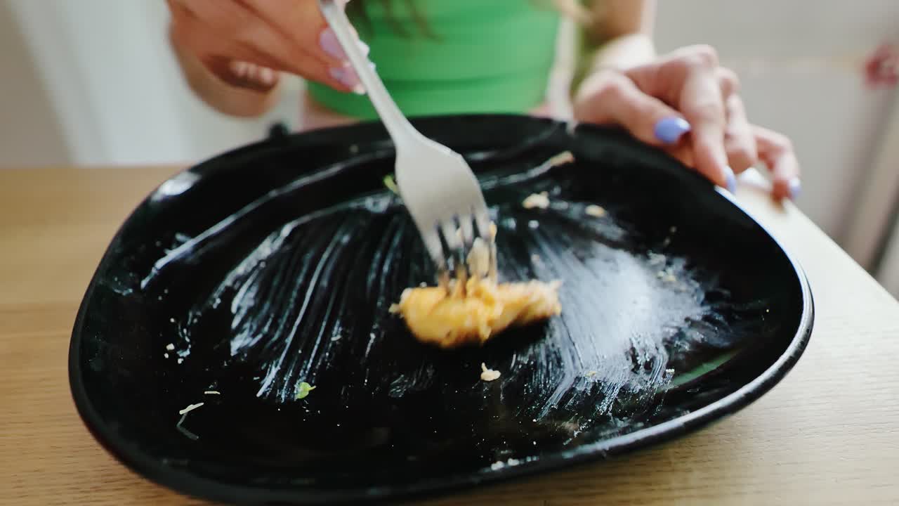 Domestic kitchen moment, woman in green shirt eating final bite of chicken