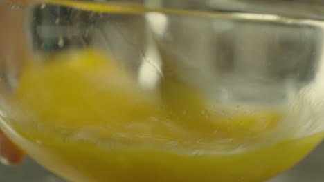 Close-up-of-whisking-eggs-in-a-glass,-transparent-bowl-using-a-fork