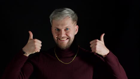 smiling man in stylish blouse looking approvingly at camera showing thumbs up on black background