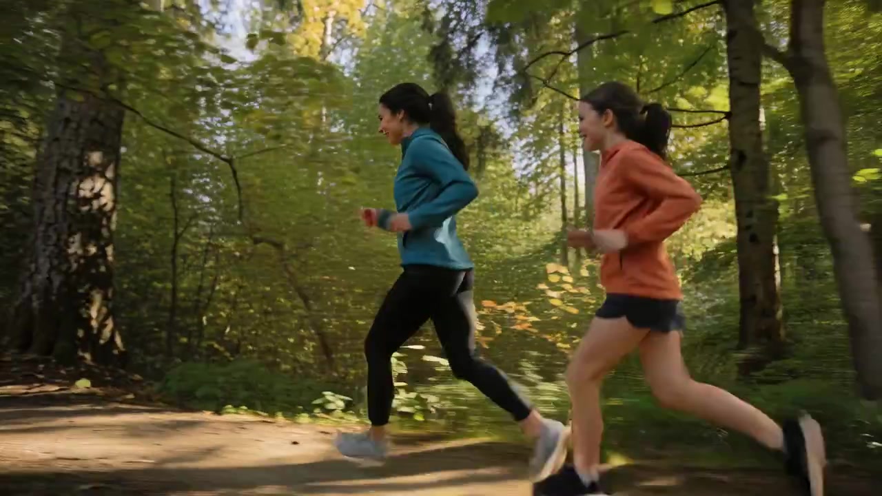 Due donne che corrono, motivate da un incontro, allenandosi su un sentiero nel bosco con giacca verde acqua e felpa con cappuccio arancione.