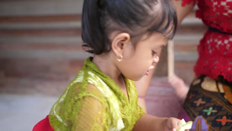 adorable little indonesian girl makes a flower decoration from strips of palm leaves and staples the final product