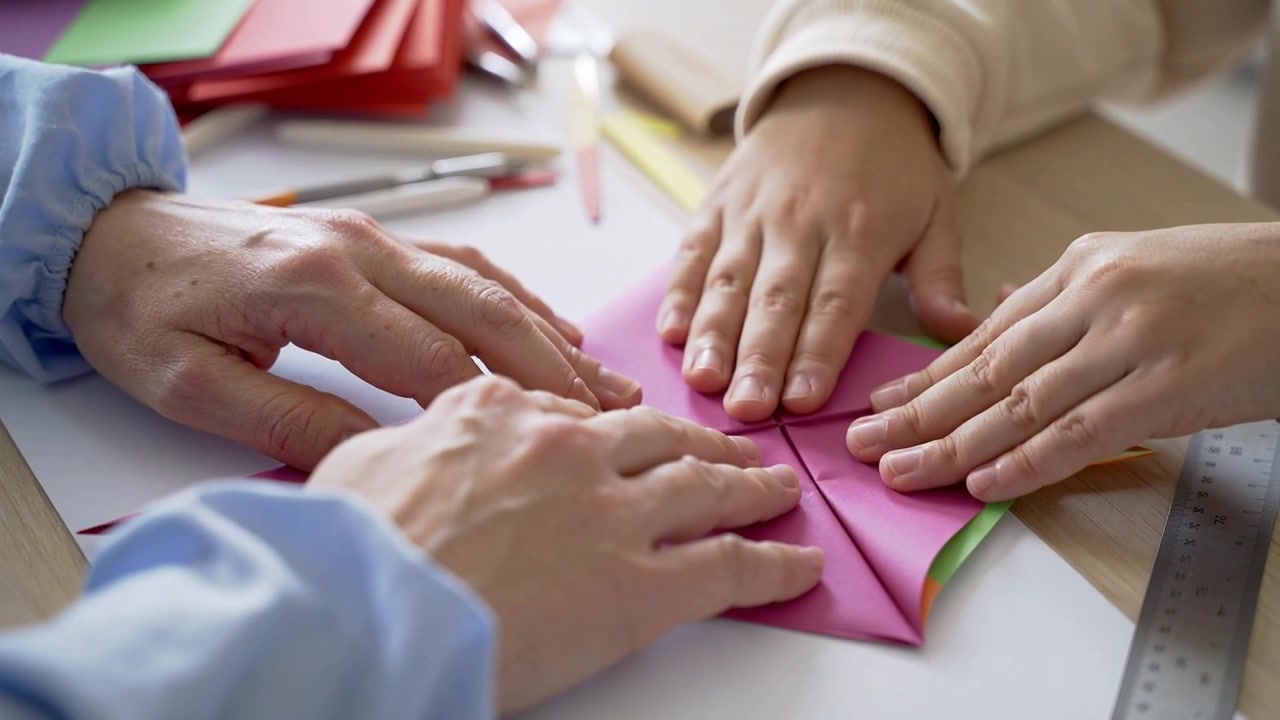 Positioning adult hand, child folding flaps at table, pressing pink paper into symmetrical cross