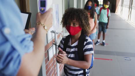 Boy wearing face mask sanitizing his hands and getting his  temperature checked