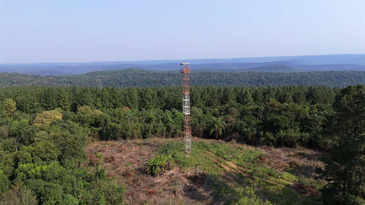 Metal fire lookout tower rising above forest landscape, providing a crucial vantage point for detecting and monitoring wildfires, ensuring response and protection of natural resources drone pull out