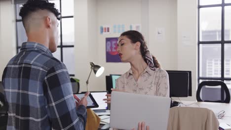 dos diseñadores creativos felices y diversos en discusión en una tableta en una oficina casual, cámara lenta
