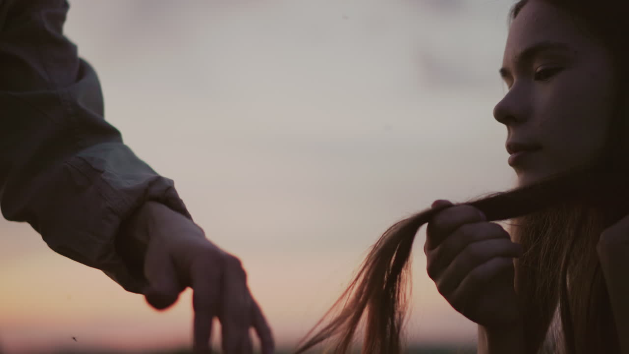 close up of hands holding lighter burning hair tip of young woman while water pours to quench glowing ember against soft sunset field background