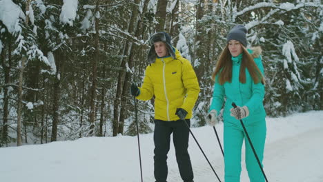 smiling girl in blue jacket skiing rides in the woods with her boyfriend in winter on the eve of valentine's day. slow motion.