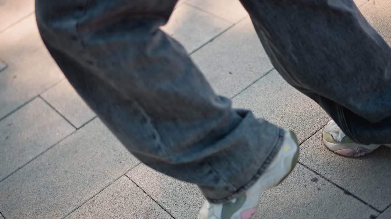 street dancer footwork on pavement, jeansclad legs executing precise steps, rhythmic heeltoe motion, dynamic balance and flow, rehearsal energy, urban stage under soft sunlight, focused foot