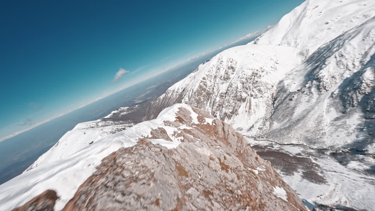 drone fpv volando sobre la cresta de la montaña cubierta de nieve en un día despejado