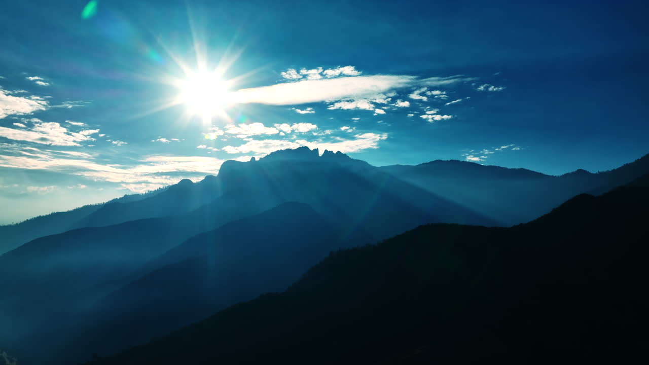 Sun shining bright above the mountains. Black and blue silhouettes of rocks in California.