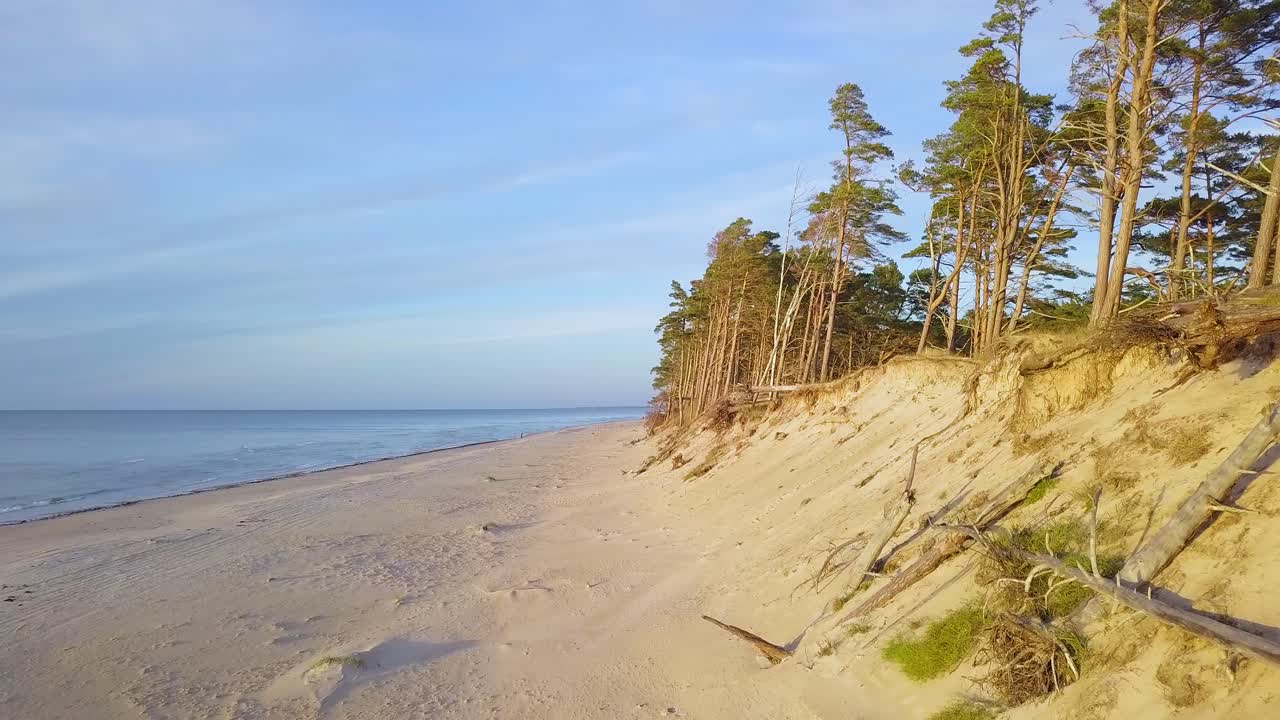 Beautiful aerial establishing view of Baltic sea coast on a sunny evening, golden hour, beach with white sand, coastal erosion, climate changes, wide angle drone shot moving backward