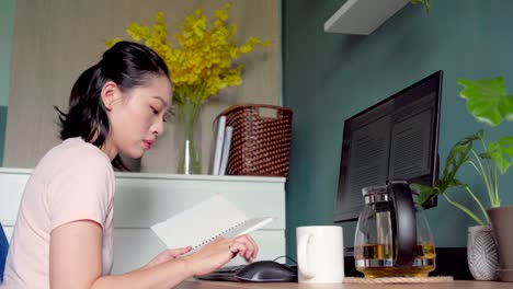 Asian-woman-reading-notes-in-notepad-and-working-from-home