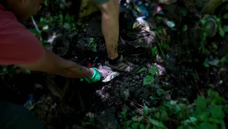 man volunteer with gloves picking and pulling garbage stuck on the ground in the forest of manali, himachal pradesh, india. save the planet concept.  - high angle shot