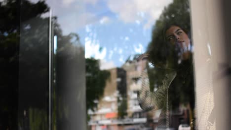 a nice shot through a window. girl walks by and checks her reflection and does here hair. after that she walks away.