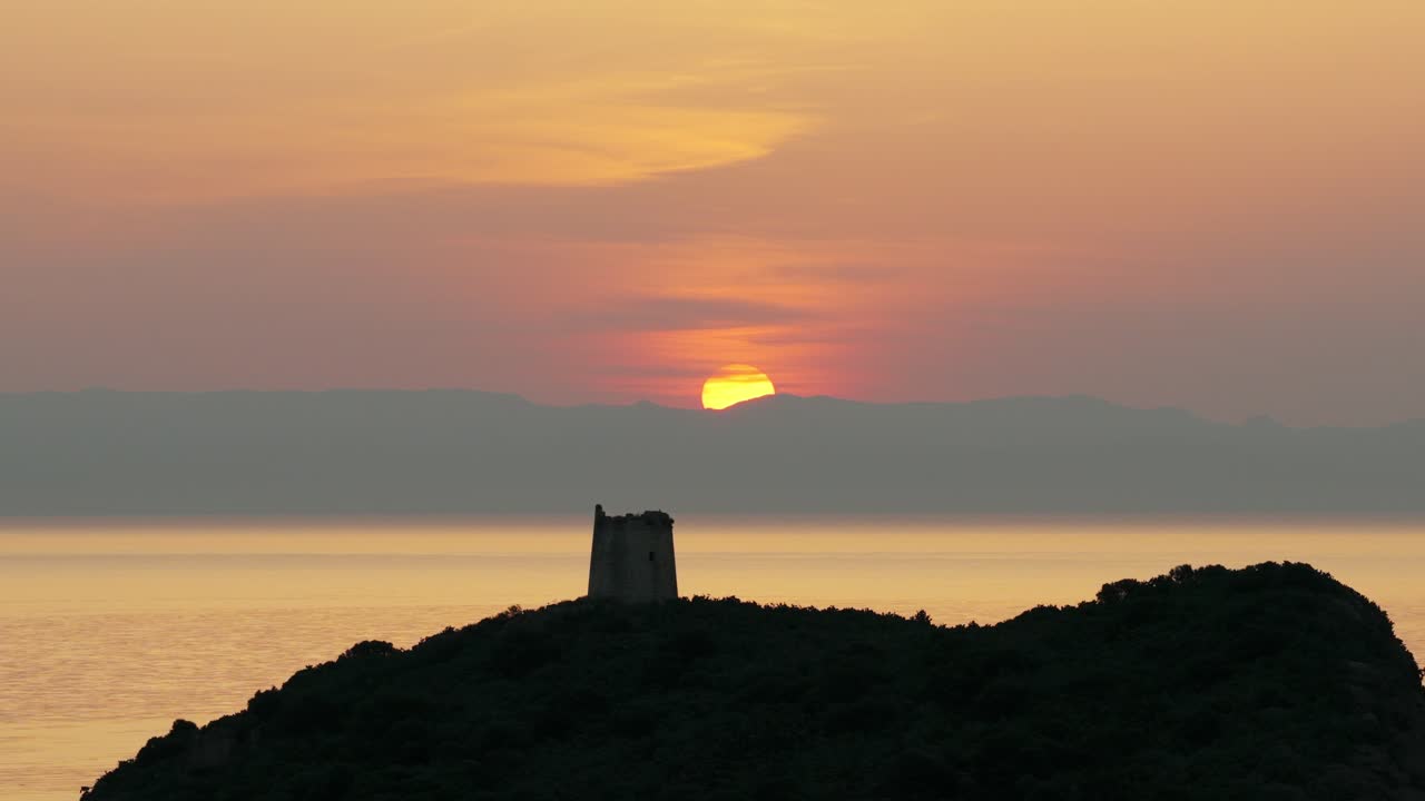 San Macario island and tower with setting sun in background, Pula, Sardinia, Italy. Aerial drone lateral view