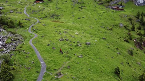 Hiker-people-at-Kandersteg-Oeschinen-Lake-on-green-alpine-meadows-by-a-creek-and-mountain-hut-amid-swiss-alps