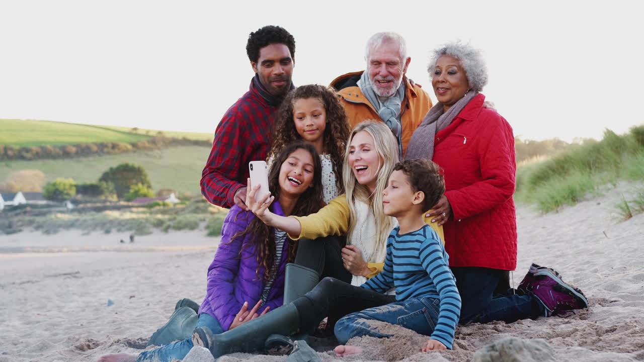 Flergenerationsfamilie sidder ved et bål på vinterstrandferie og tager en selfie.