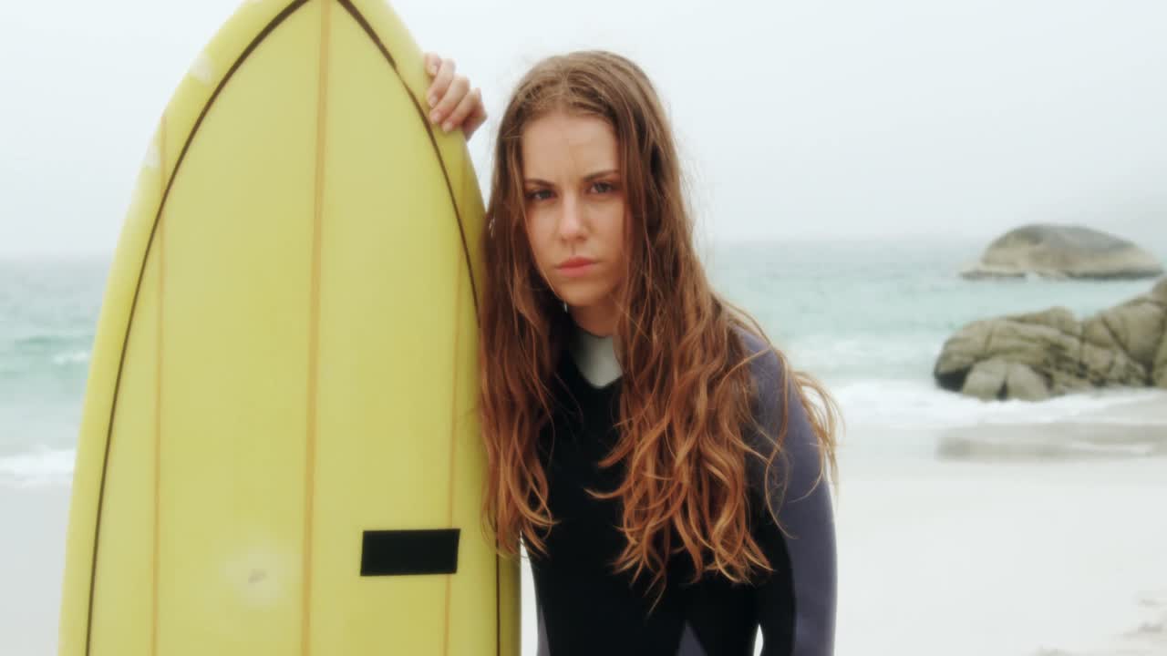 해변 4k에 서핑 보드와 함께 서 있는 코카시안 여성 서퍼의 앞면