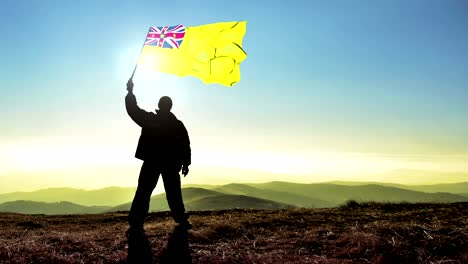 hombre de silueta exitoso ganador agitando la bandera de niue en la cima de la montaña, fondo de bucle de cinemagraph