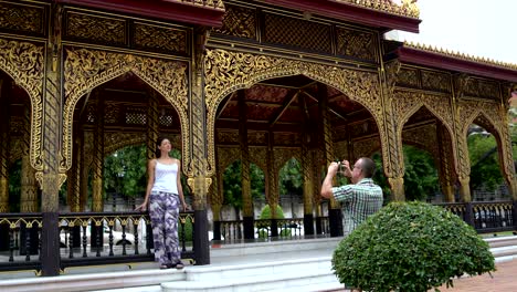 a man is taking pictures on a smartphone of a woman next to a beautiful metal carved arbor