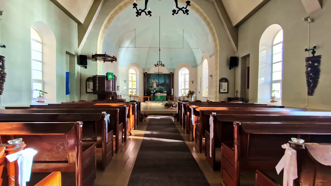 Warm morning light fills the wooden pews and arched windows inside Lielvārde church. Lielvārde, Latvia