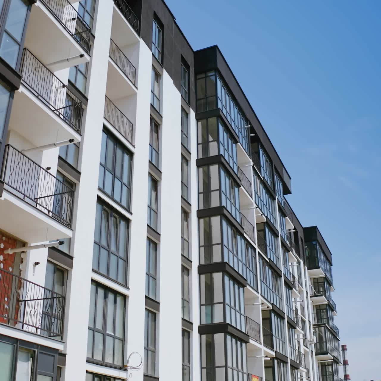Modern facade of multi-storied-building. New apartment building in black and white colors against blue sky. Drone view