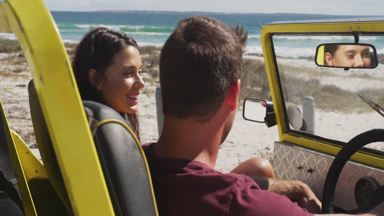 feliz pareja caucásica sentada en un buggy de playa junto al mar hablando