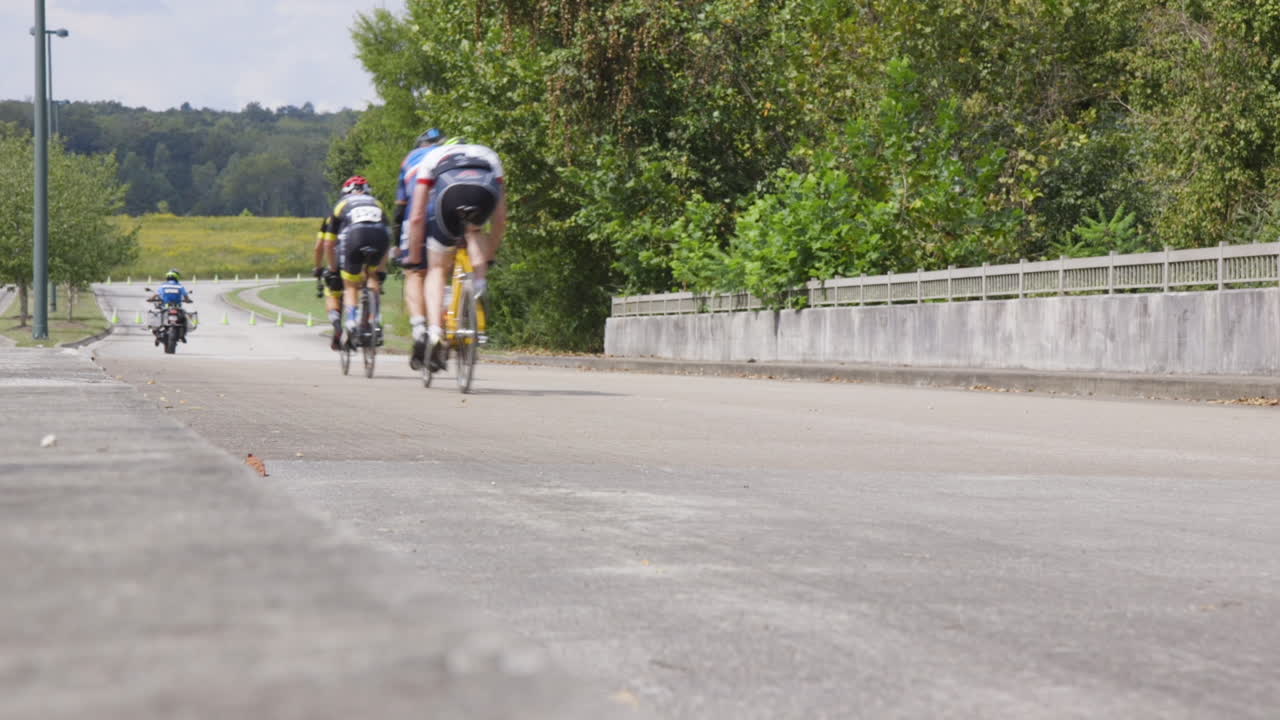 The lead motorcycle and a number of tandem bicycles cycle past the camera during a para-cycling race