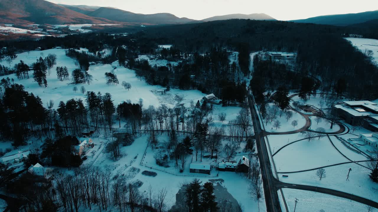 rotación de alta altitud en la cabaña cubierta de nieve entre maderas duras y árboles de hoja perenne rodeados de campos con luz suave de un cielo oscuro