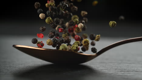 colorful pepper blend on a copper tablespoon falling onto stone tabletop in slow motion and macro